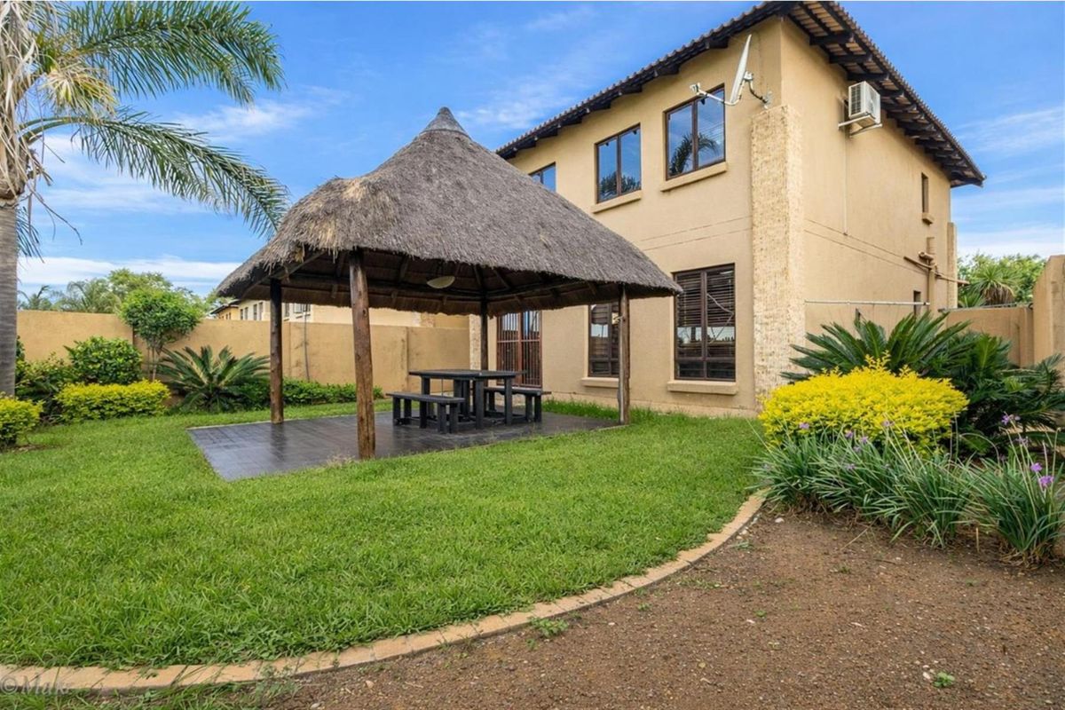 Rear view of the townhouse featuring a landscaped garden, a thatched gazebo, and a paved patio area.