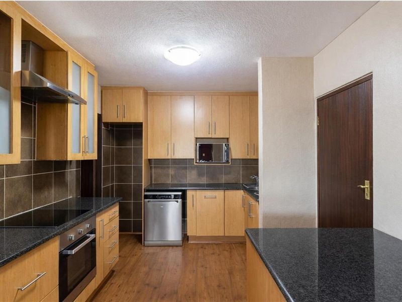A functional kitchen featuring light wood cabinetry, dark granite countertops, a built-in oven, extractor fan, and integrated dishwasher space.