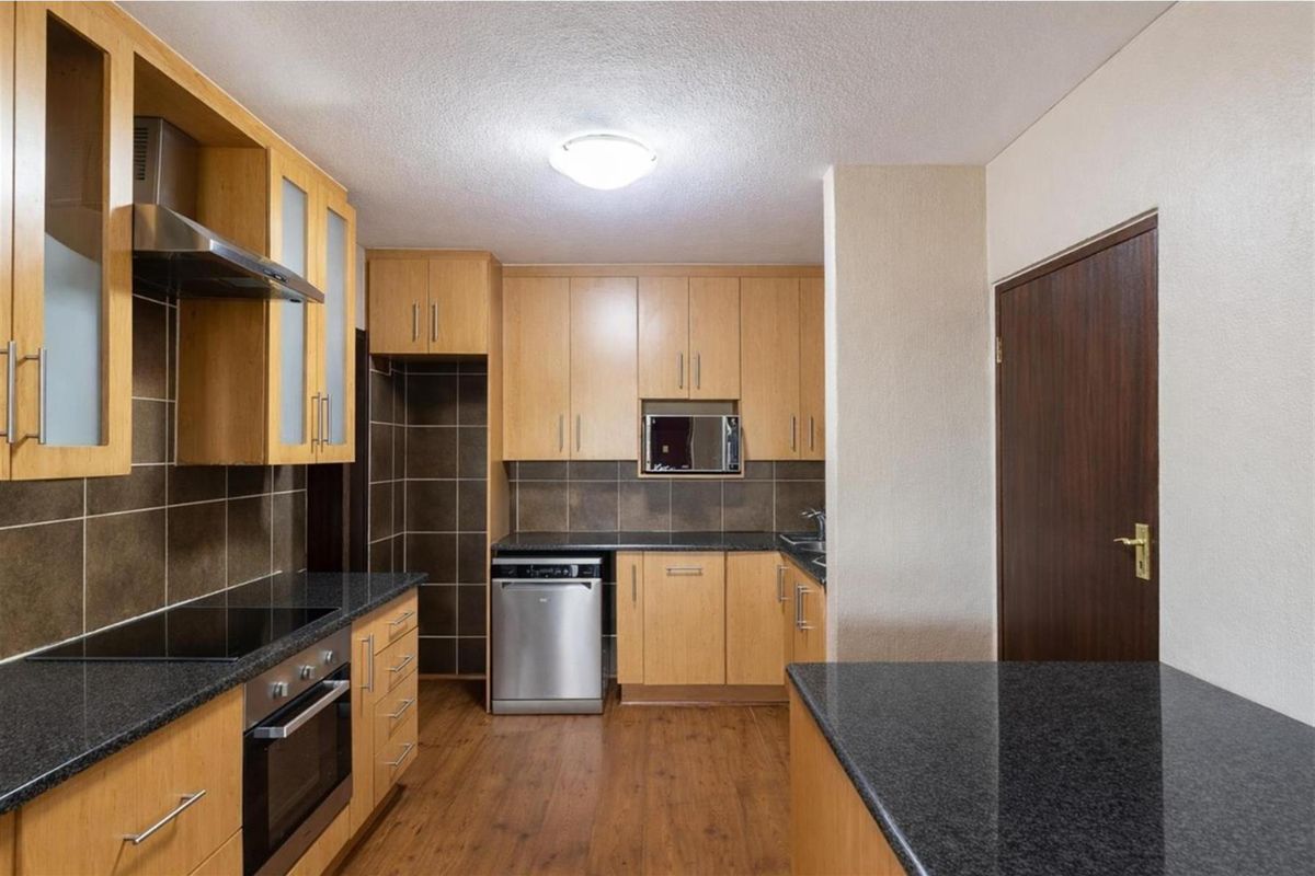 A functional kitchen featuring light wood cabinetry, dark granite countertops, a built-in oven, extractor fan, and integrated dishwasher space.