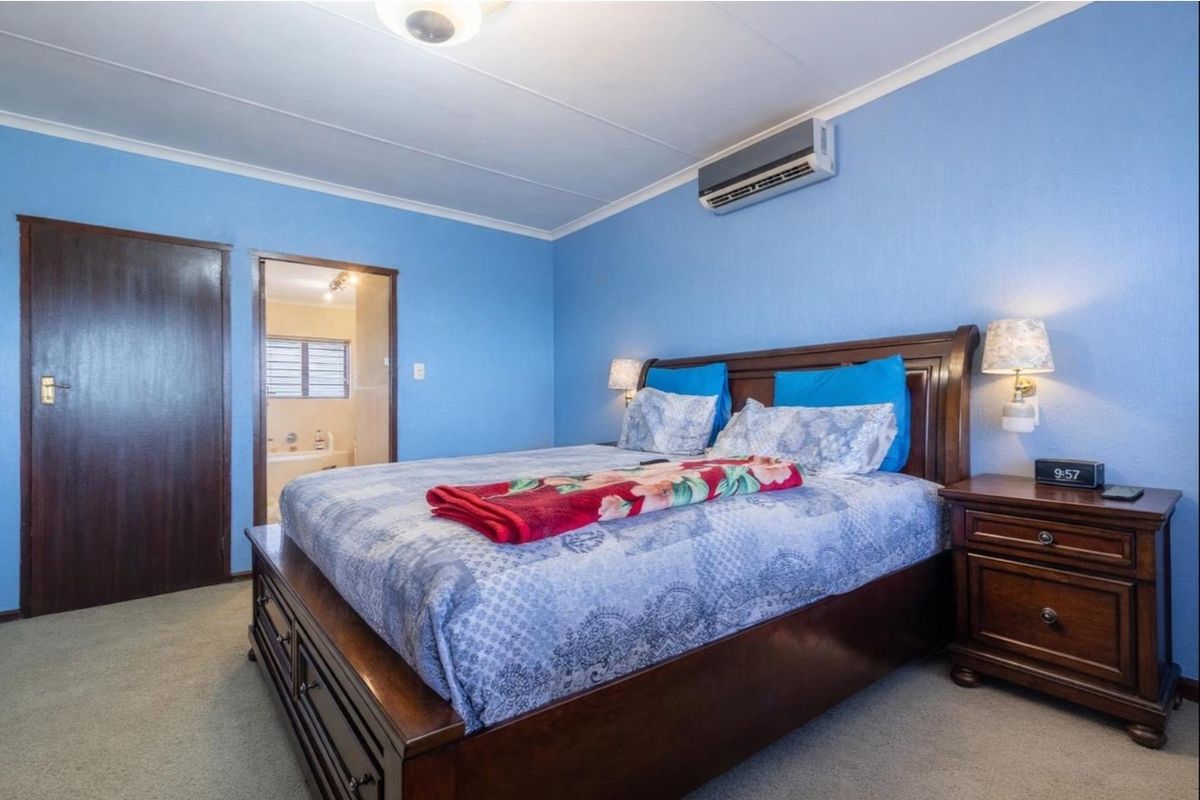 A bedroom featuring blue walls, carpeted flooring, a wall-mounted air conditioning unit, and an en-suite bathroom access.