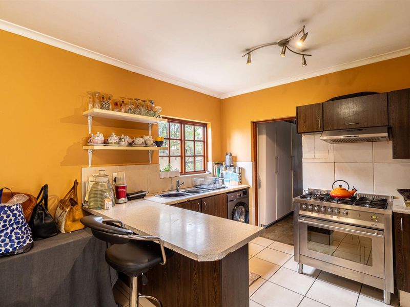A functional kitchen featuring dark wood cabinetry, a stainless steel gas stove with extractor fan, tiled flooring, and a breakfast counter.