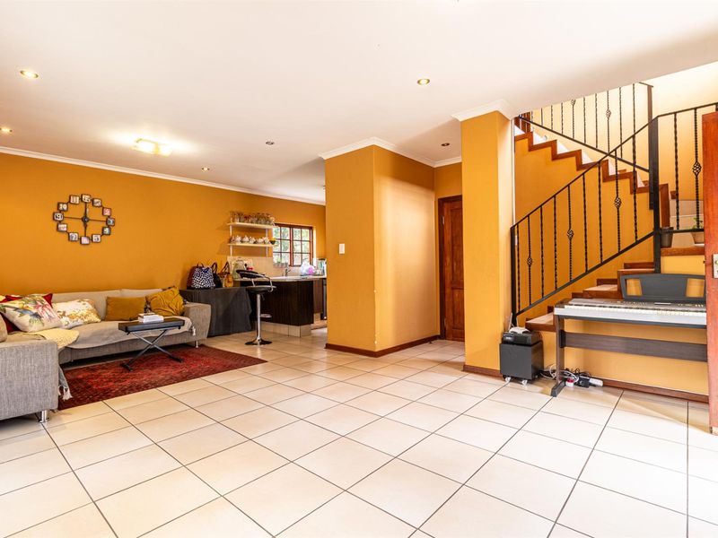 Open plan living area featuring tiled flooring, a staircase with wrought iron balustrade, and a partial view into the kitchen area.