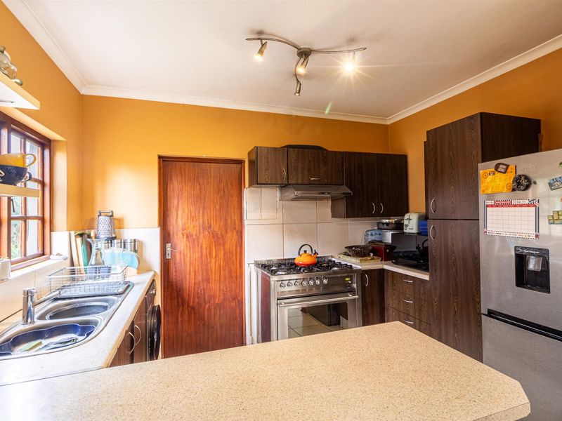 A functional kitchen featuring dark wood cabinetry, a stainless steel gas stove with extractor fan, double basin sink, and a breakfast counter.