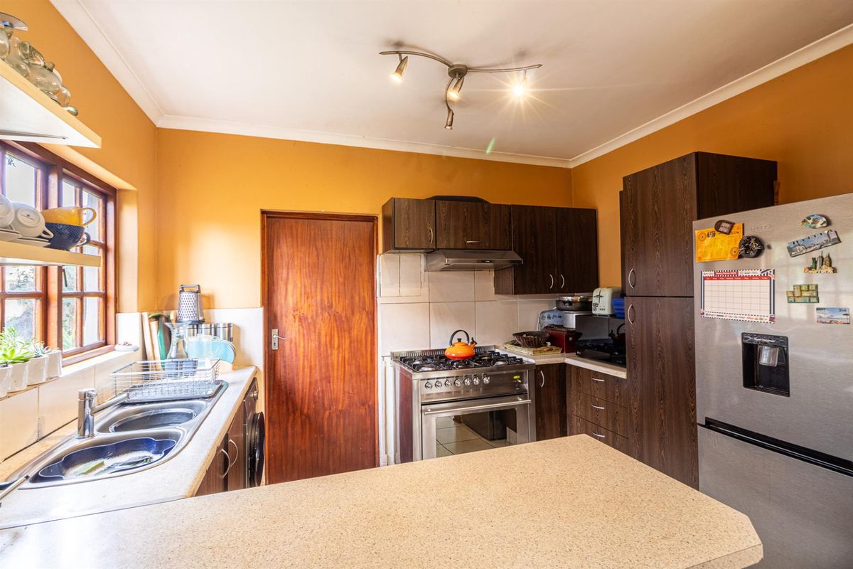 A functional kitchen featuring dark wood cabinetry, a stainless steel gas stove with extractor fan, double basin sink, and a breakfast counter.