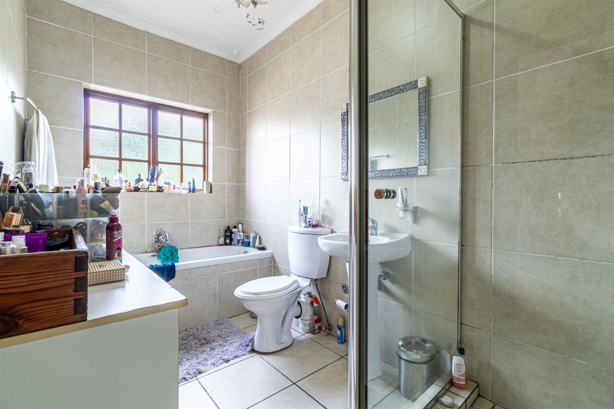 A dated bathroom featuring a built-in bathtub, pedestal basin, and a glass-enclosed shower with neutral wall and floor tiling.