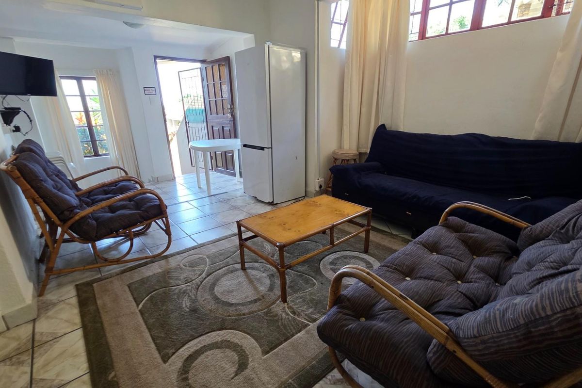 A functional living room area featuring tiled flooring, natural light through multiple windows, and direct access to an exterior entrance.