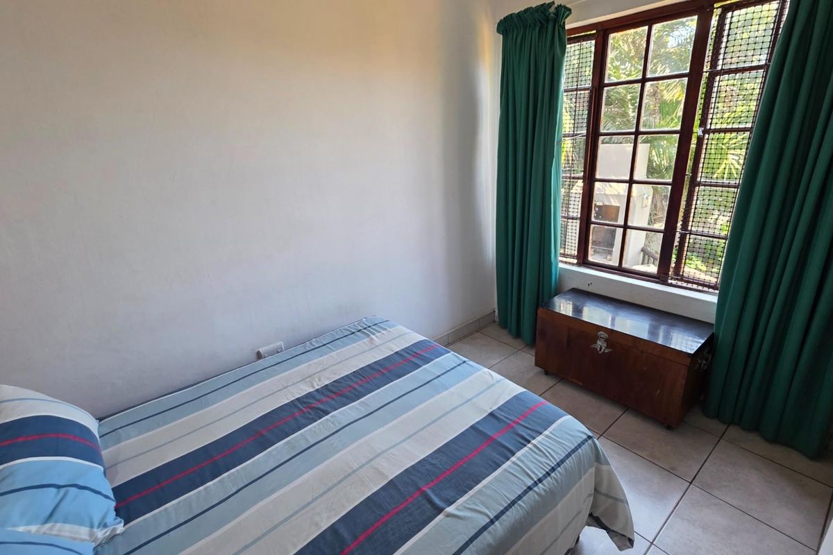 A bedroom featuring tiled flooring, a large window with security bars, and green curtains, providing natural light and a view of the outdoor area.