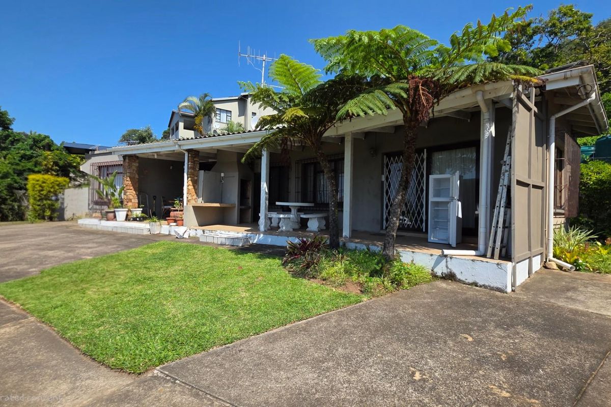 A rear view of the house featuring a covered patio area, concrete driveway, and established garden space.