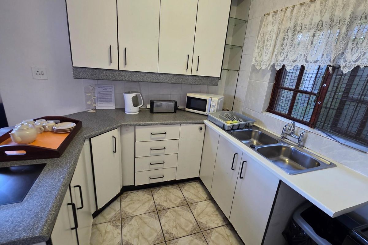 A functional kitchen featuring white cabinetry, laminate countertops, a double stainless steel sink, and tiled flooring.