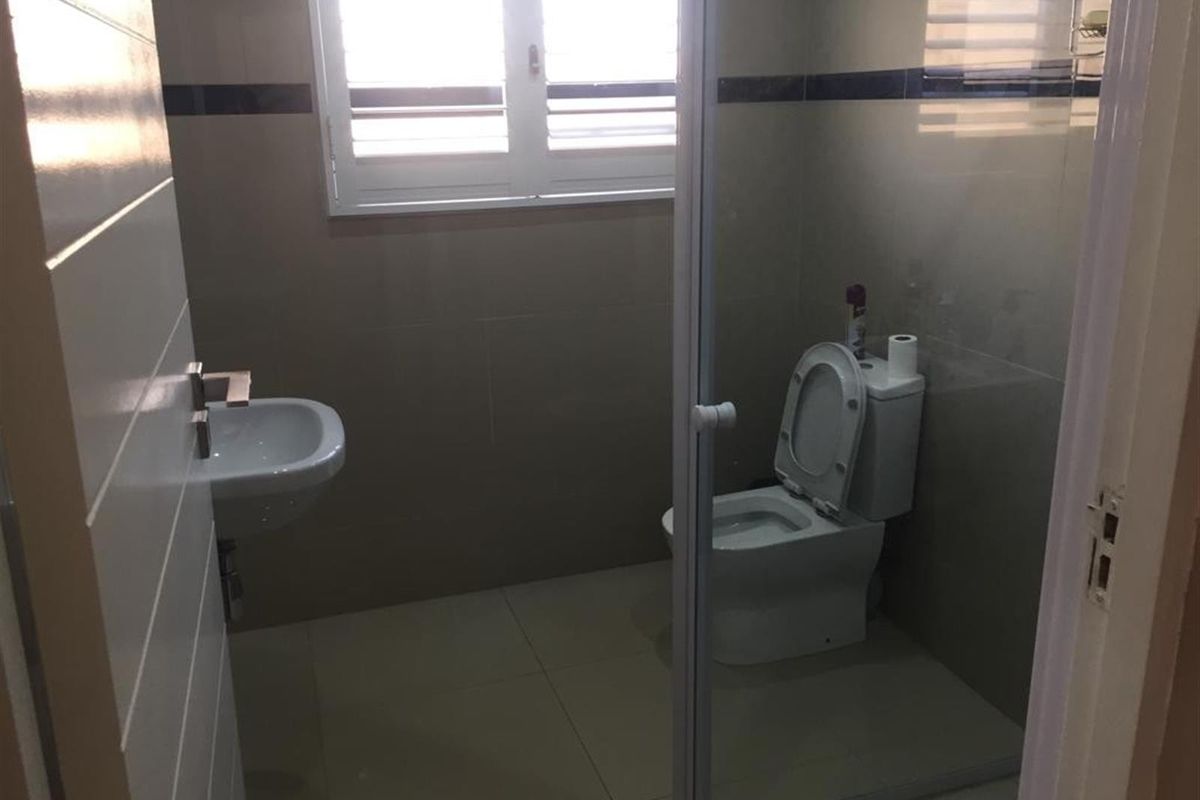 A clean, functional bathroom featuring tiled walls and flooring, a wall-mounted basin, and a toilet, with natural light provided by a window.