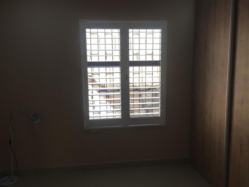 A simple bedroom featuring a built-in wardrobe and a window fitted with security bars and shutters.
