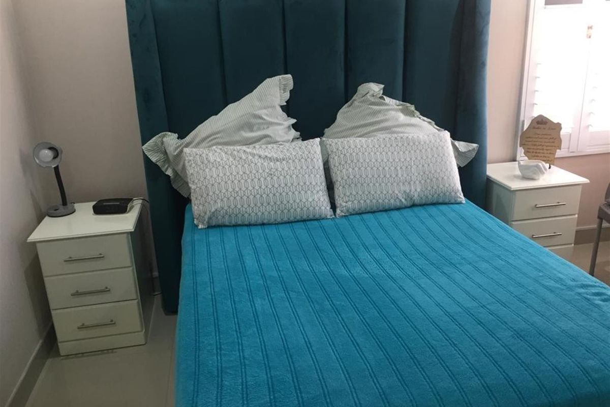 A bedroom featuring a tall upholstered headboard and white bedside tables with integrated window shutters.