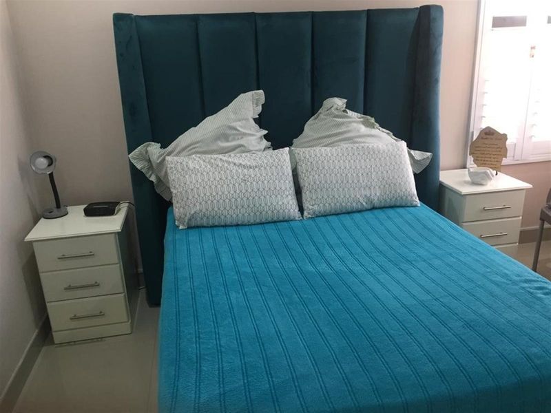 A bedroom featuring a tall upholstered headboard and white bedside tables with integrated window shutters.