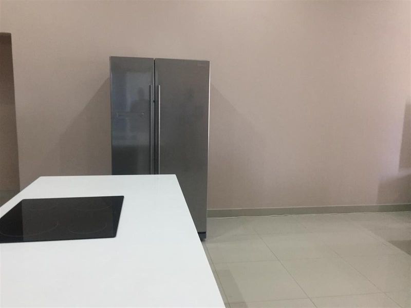 A minimalist kitchen area featuring a central island with an integrated cooktop and neutral tiled flooring.