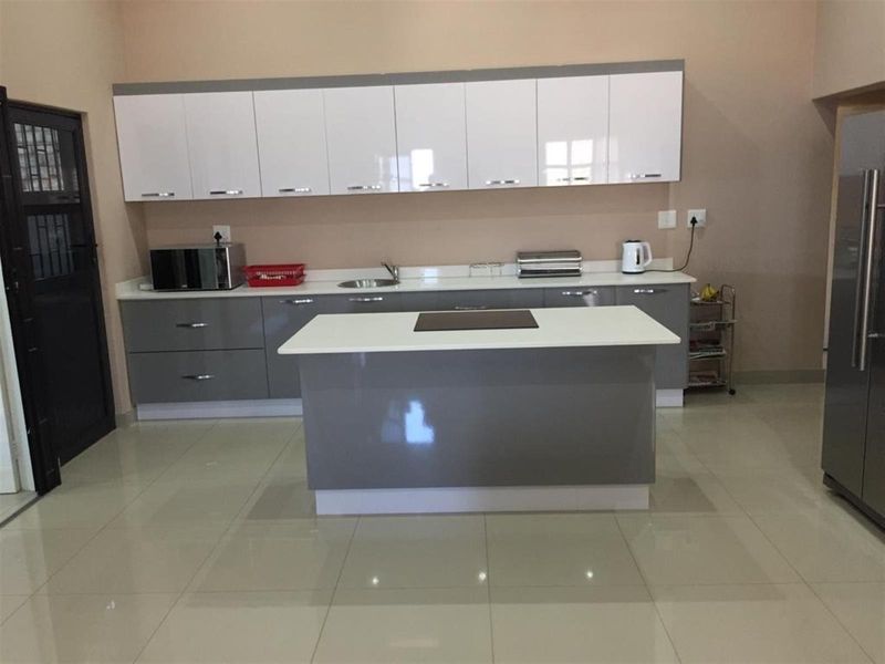 Modern kitchen featuring high-gloss grey and white cabinetry, a central island with a stone countertop, and polished tiled flooring.