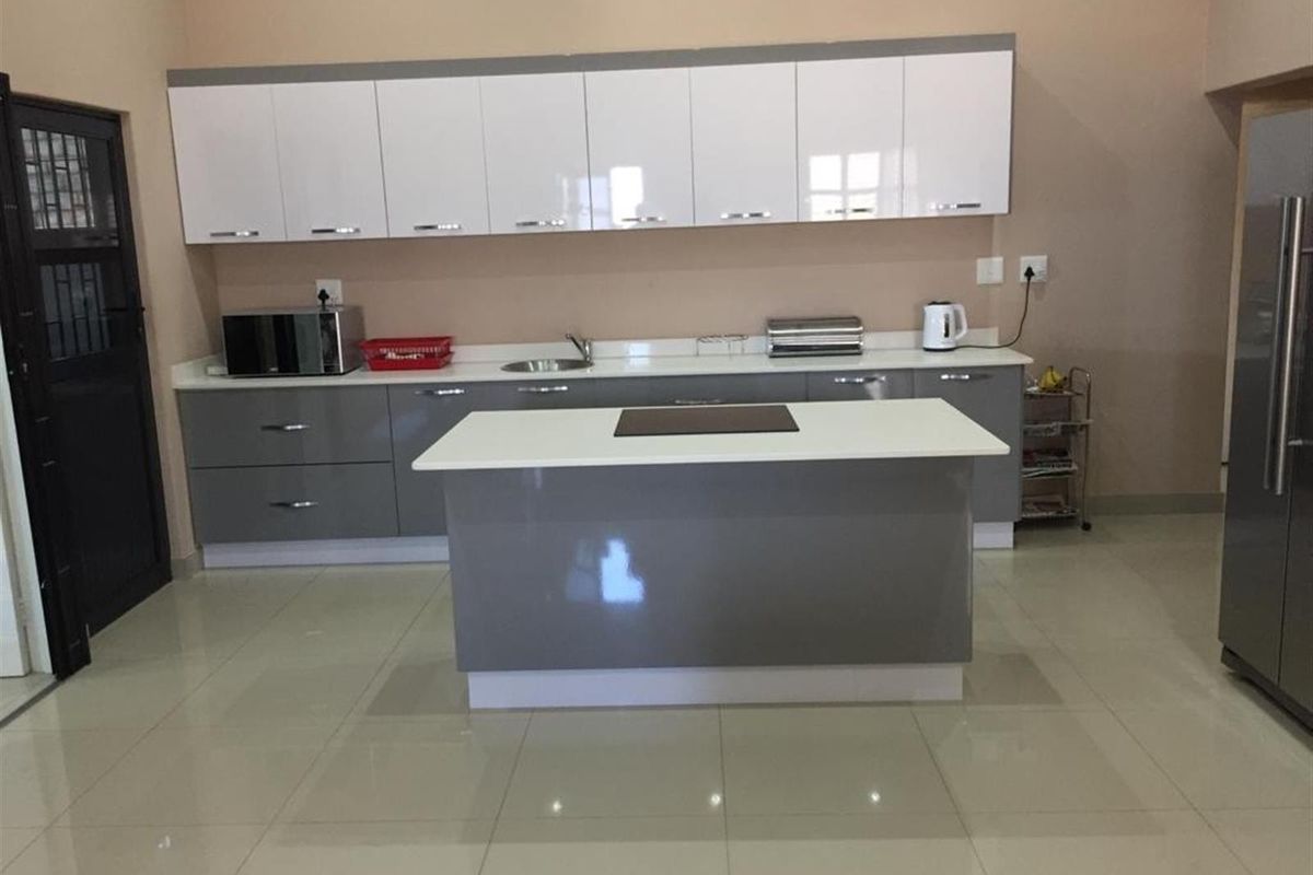 Modern kitchen featuring high-gloss grey and white cabinetry, a central island with a stone countertop, and polished tiled flooring.