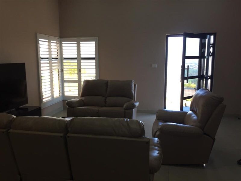 A living room featuring tiled flooring, plantation shutters, and a glass door providing access to the exterior.