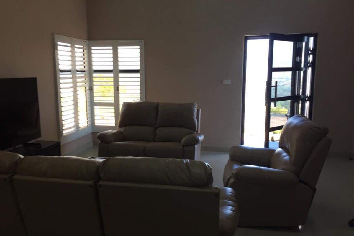 A living room featuring tiled flooring, plantation shutters, and a glass door providing access to the exterior.
