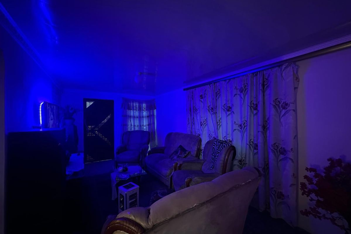 A living room space featuring a security gate at the entrance and curtained windows, currently illuminated by strong blue ambient lighting.