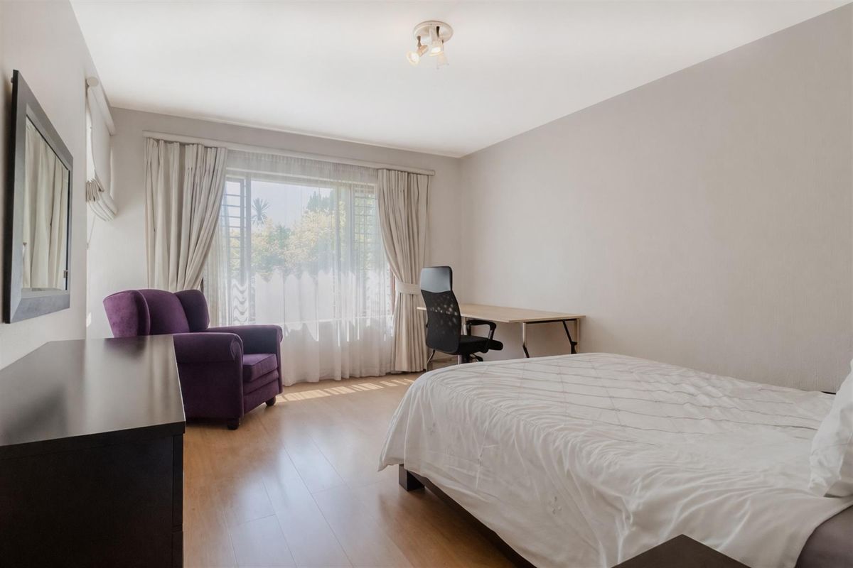 A bright and spacious bedroom featuring light wood-look flooring, large windows with curtains, and a neutral color palette.