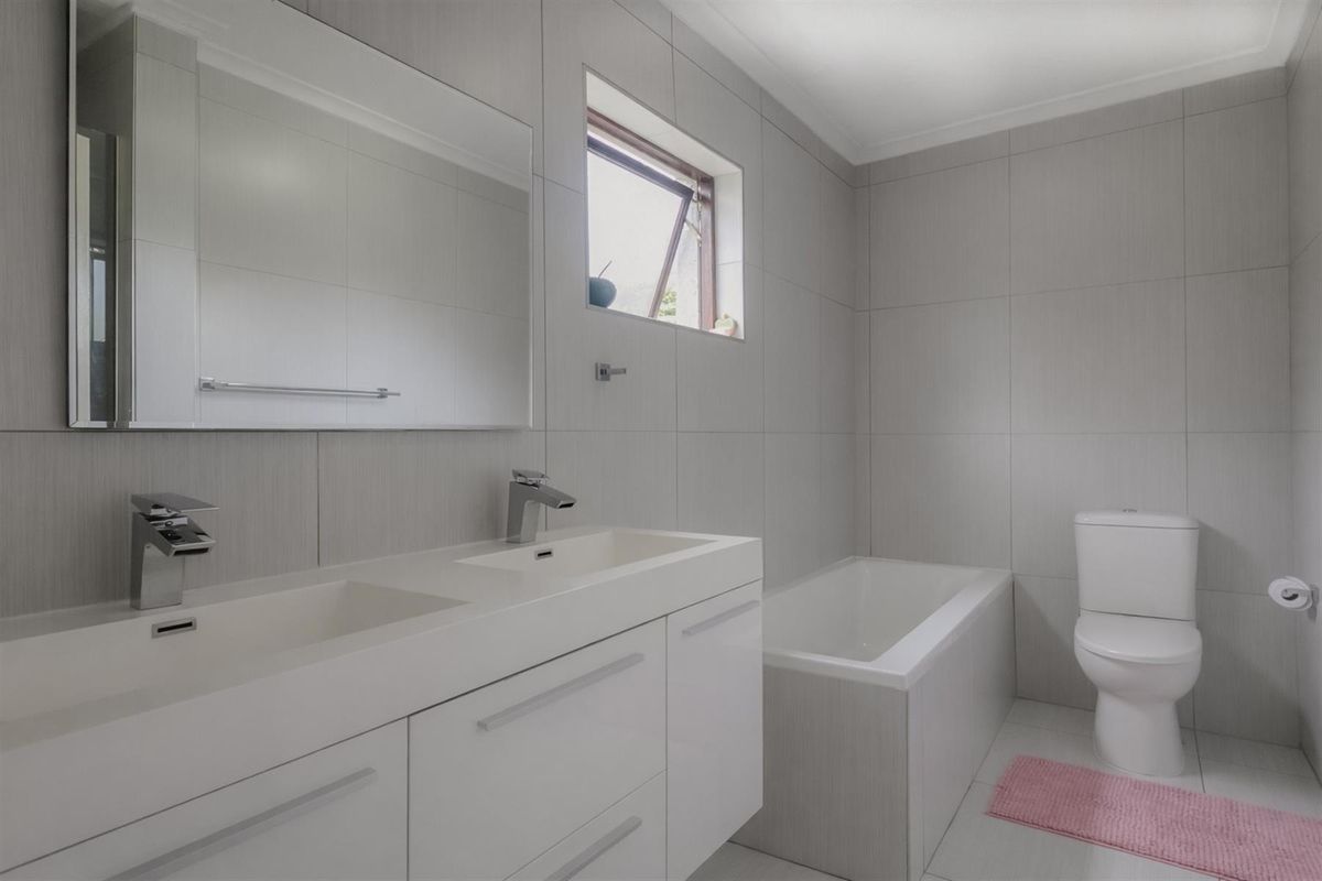 Modern bathroom featuring a double vanity with integrated sinks, a built-in bathtub, and neutral wall tiling.