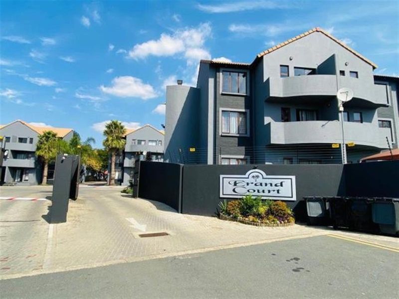 Front entrance view of Grand Court apartment complex featuring a paved driveway, security gate, and perimeter electric fencing.