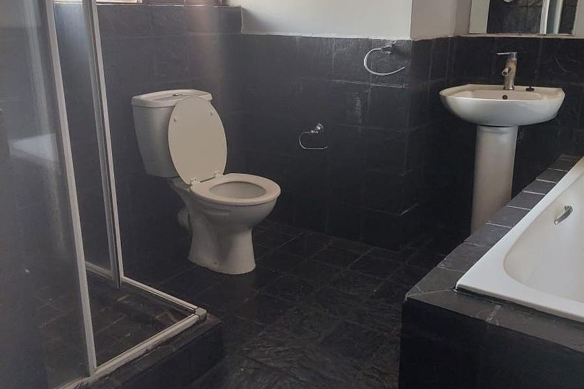 A functional bathroom featuring a pedestal basin, built-in bathtub, separate shower enclosure, and dark tiled finishes throughout.