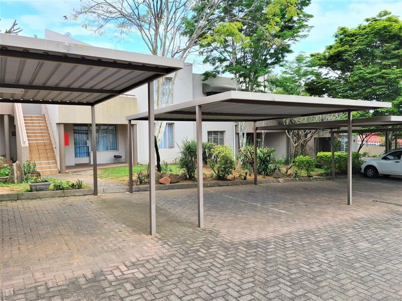 Exterior view of the apartment complex featuring paved parking areas with covered carports and landscaped garden surrounds.