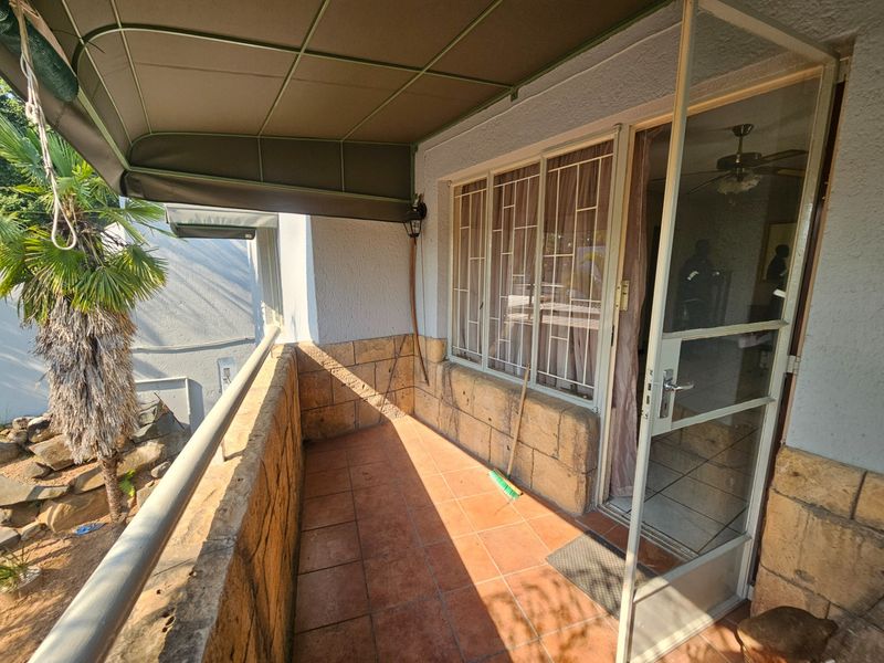 A covered balcony featuring tiled flooring, stone-clad walls, and a metal awning, providing a functional outdoor space with security features.