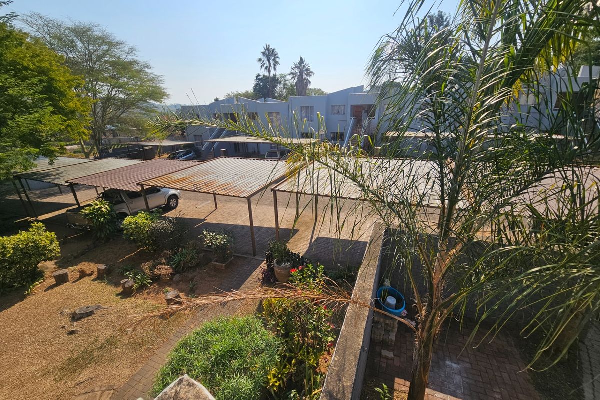 An elevated view of the apartment complex rear area, featuring paved parking bays with metal carports and landscaped garden sections.
