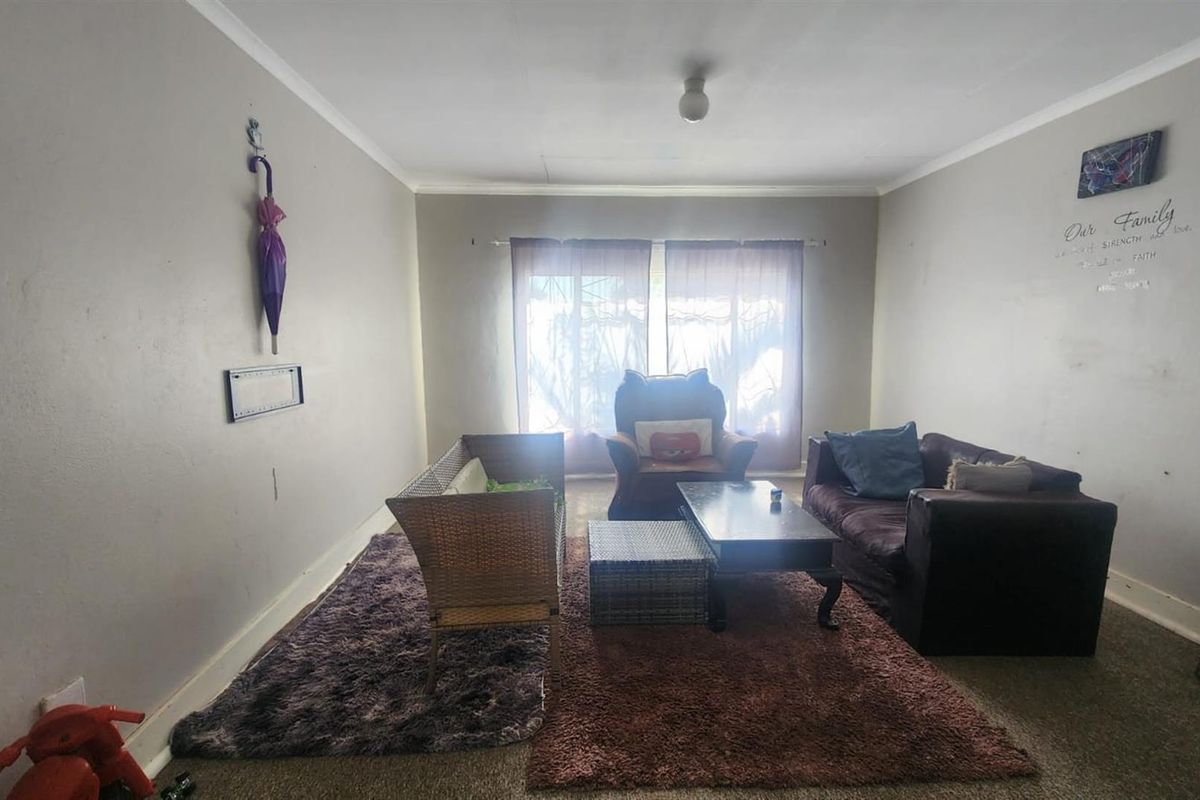 A spacious living room featuring neutral wall tones, carpeted flooring, and large windows that provide natural light.
