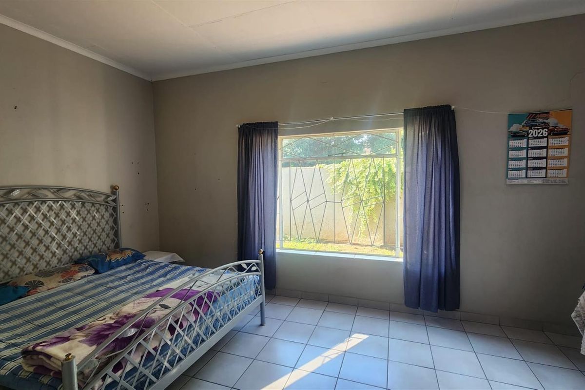 A bedroom featuring tiled flooring and a window fitted with security bars, providing natural light and a view of the exterior.