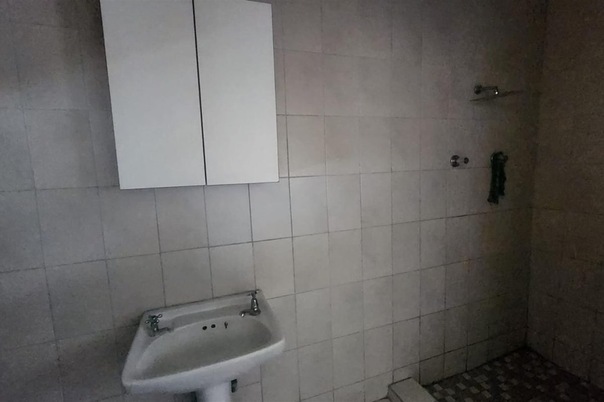 A dated bathroom featuring a pedestal basin, wall-mounted medicine cabinet, and tiled shower area with basic plumbing fixtures.