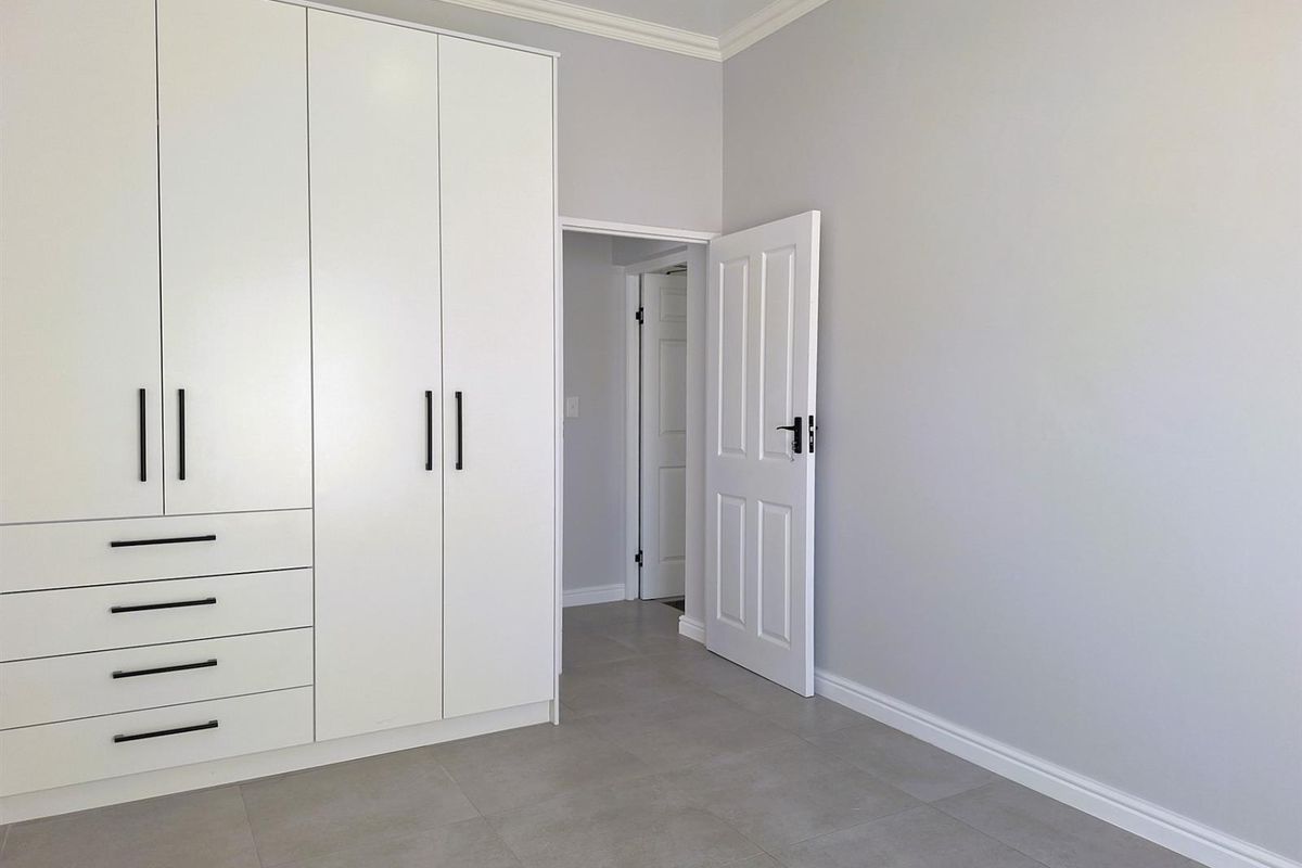 A bright, modern bedroom featuring neutral grey floor tiles, crisp white walls, and extensive built-in cabinetry with contemporary black hardware.