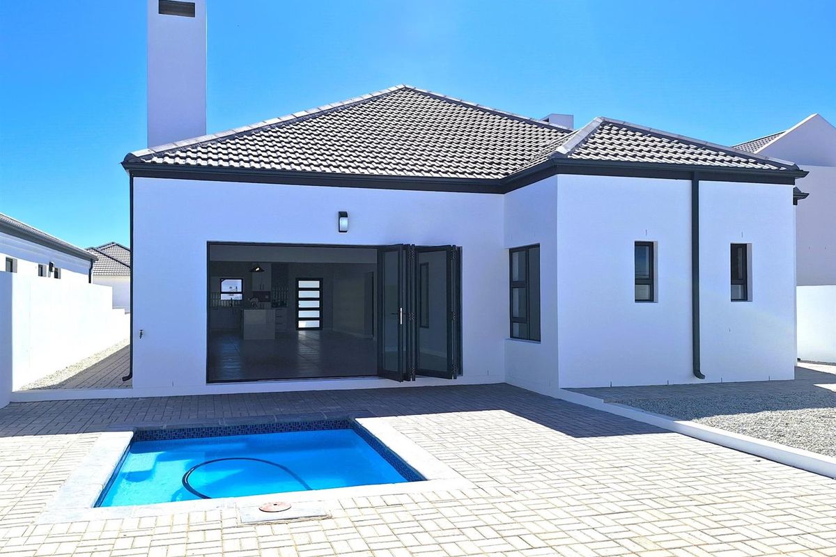 Rear view of a modern home featuring a paved patio, a private swimming pool, and large folding doors leading into the open-plan living area.