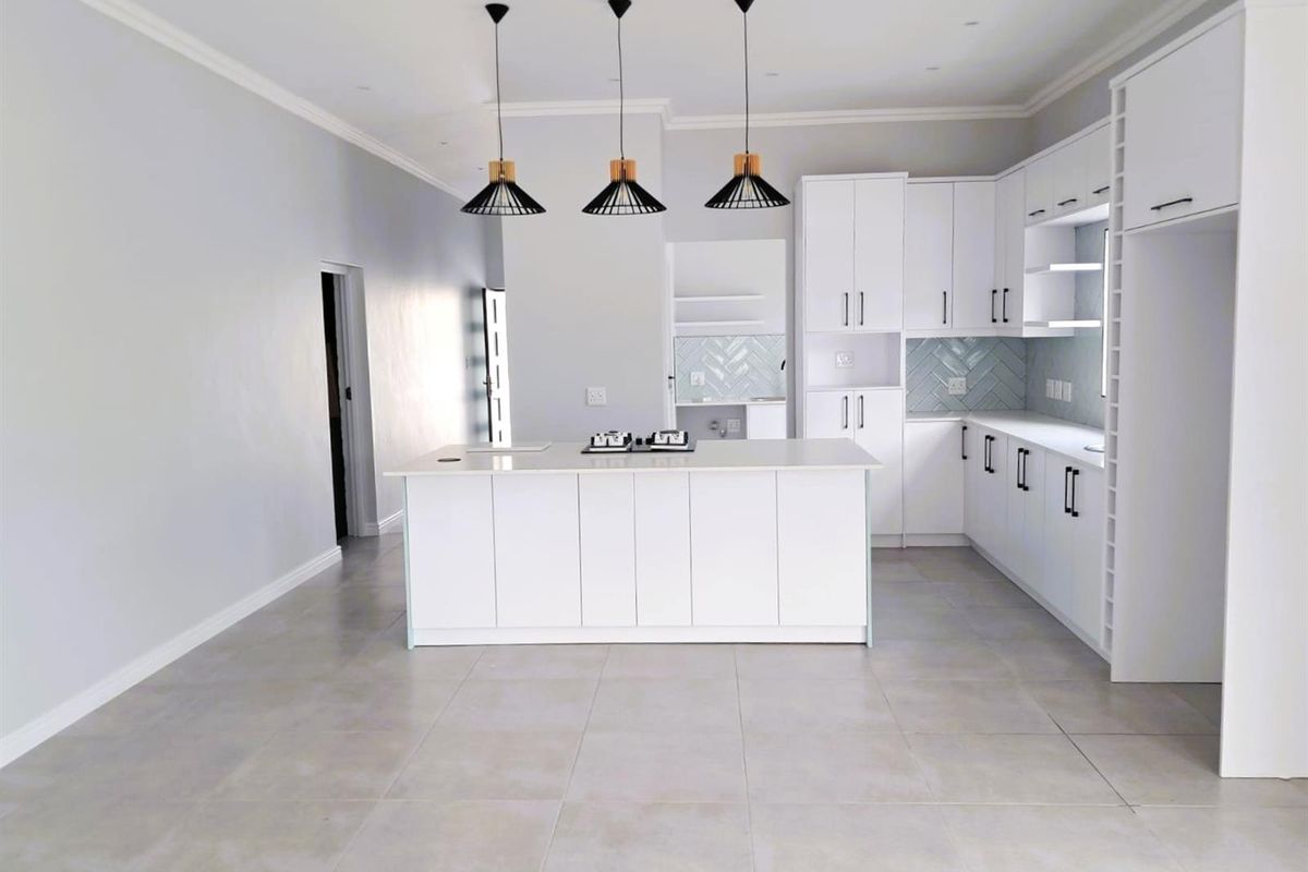 Modern open-plan kitchen featuring white cabinetry, a central island with a built-in hob, and stylish pendant lighting.