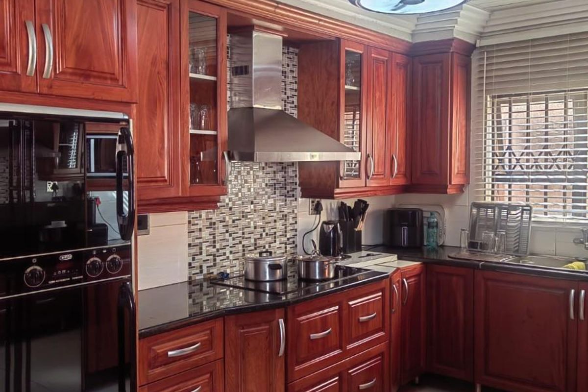 A well-maintained kitchen featuring rich wooden cabinetry, granite countertops, a mosaic backsplash, built-in appliances, and a modern ceiling fan with integrated lighting.