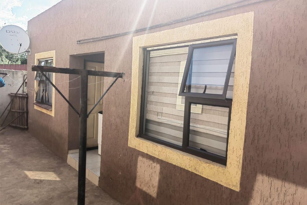 Rear exterior view of the house featuring textured wall finishes, aluminium window frames, and concrete paving.