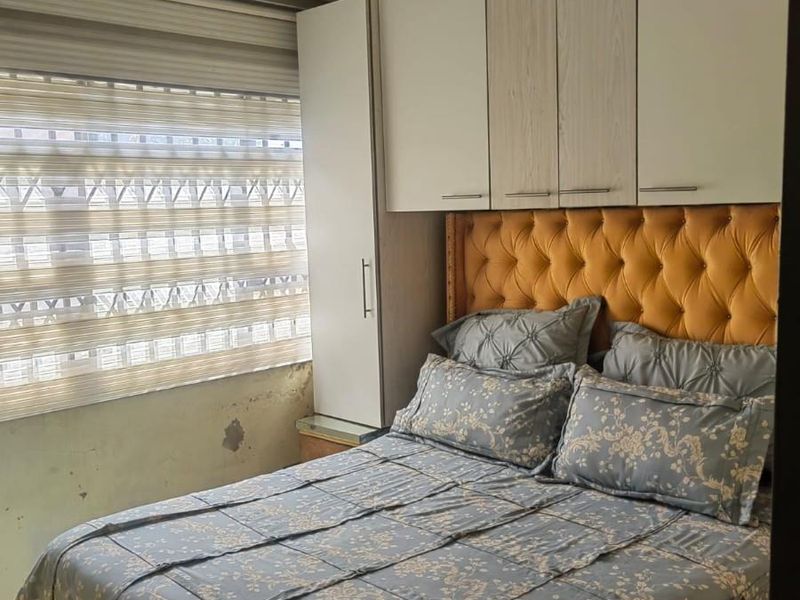 Bedroom featuring built-in overhead cabinetry and wardrobe storage, with roller blinds and a panel ceiling. Wall surface repairs are required.