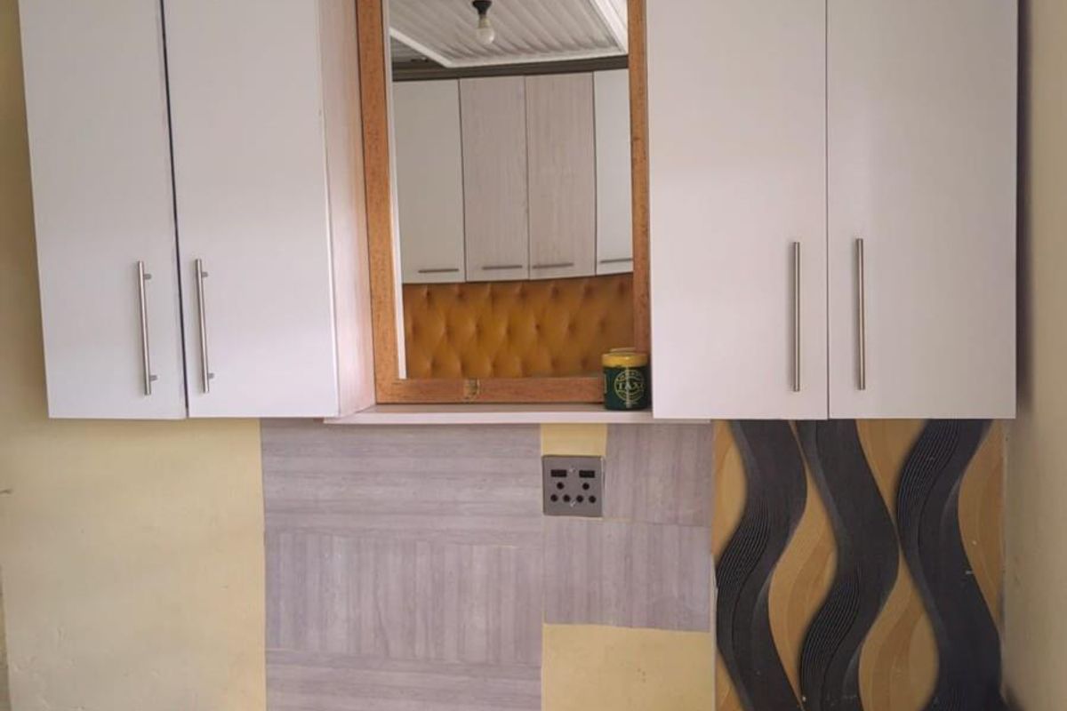 A bedroom area featuring built-in white cabinetry and a central mirror, with decorative wall paneling and an integrated electrical outlet.