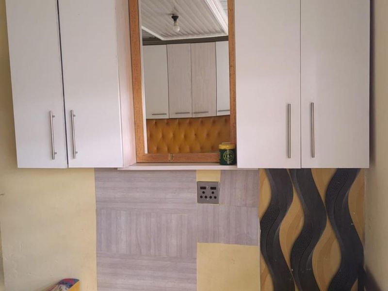 A bedroom area featuring built-in white cabinetry and a central mirror, with decorative wall paneling and an integrated electrical outlet.