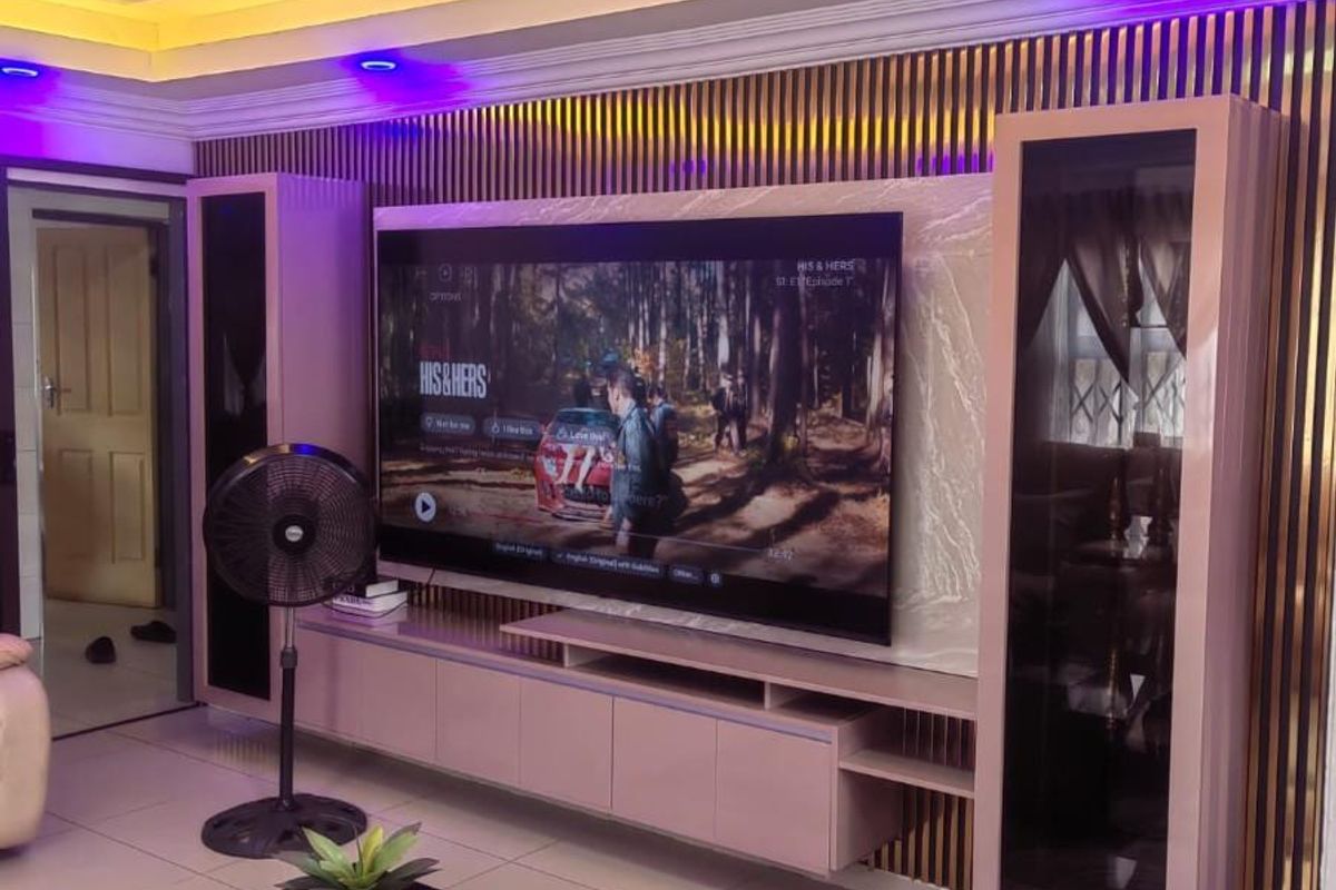 Modern living room featuring a custom built-in media wall with slatted wood accents, recessed ceiling with ambient LED lighting, and polished floor tiles.