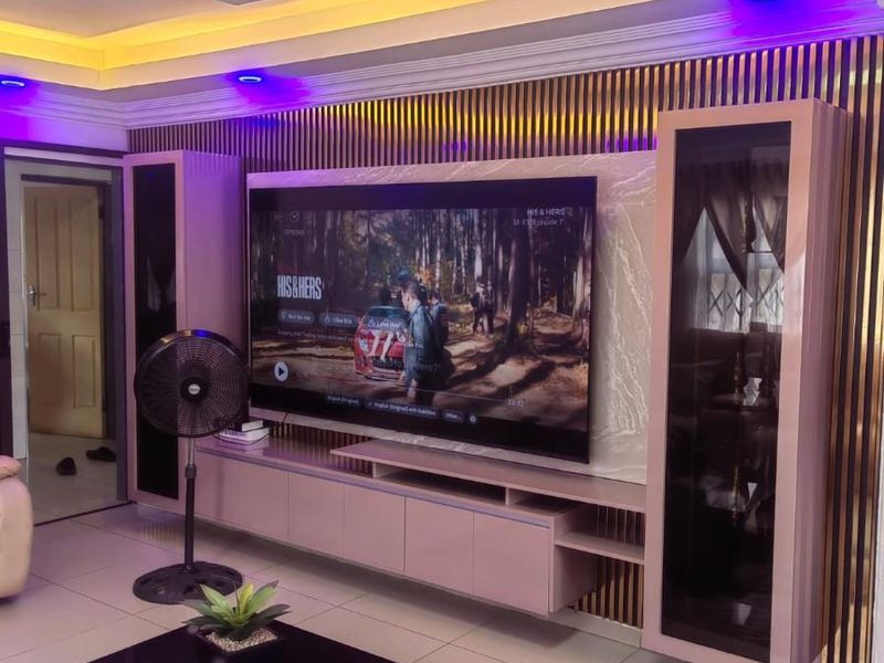 Modern living room featuring a custom built-in media wall with slatted wood accents, recessed ceiling with ambient LED lighting, and polished floor tiles.