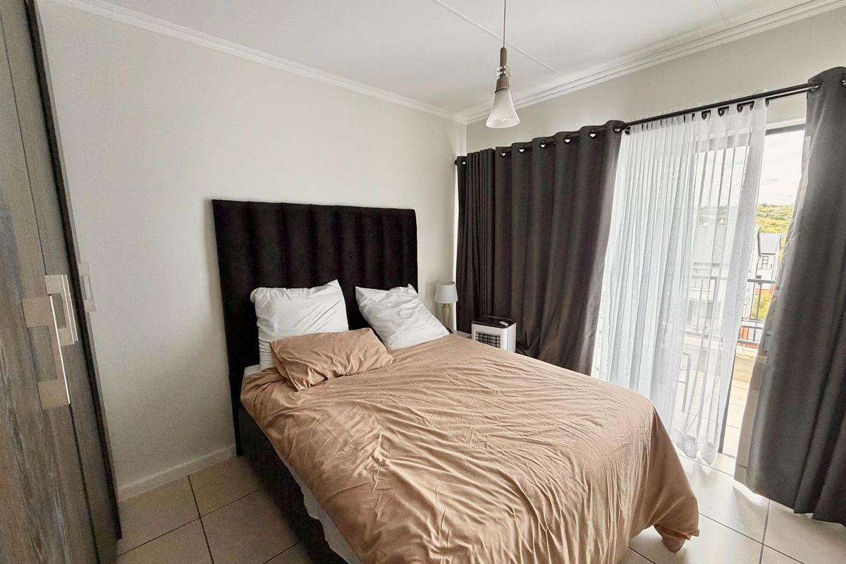 A well-lit bedroom featuring tiled flooring, a built-in wardrobe, and a sliding glass door providing access to an outdoor balcony area.