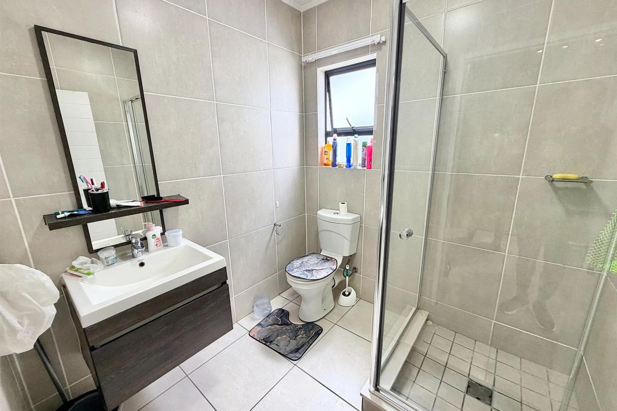 A modern bathroom featuring a wall-mounted vanity, a glass-enclosed shower, and neutral floor-to-ceiling wall tiles.