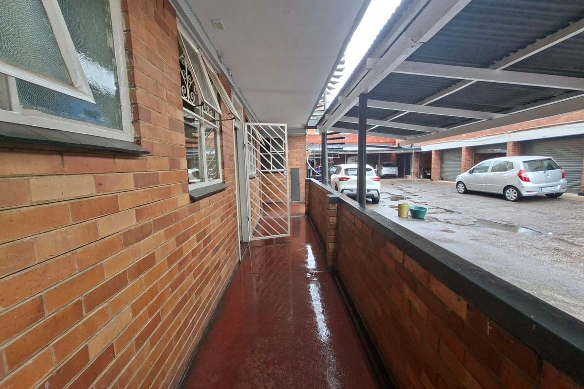 Exterior walkway featuring face brick walls, a covered roof structure, and access to the apartment entrance, overlooking the parking area.