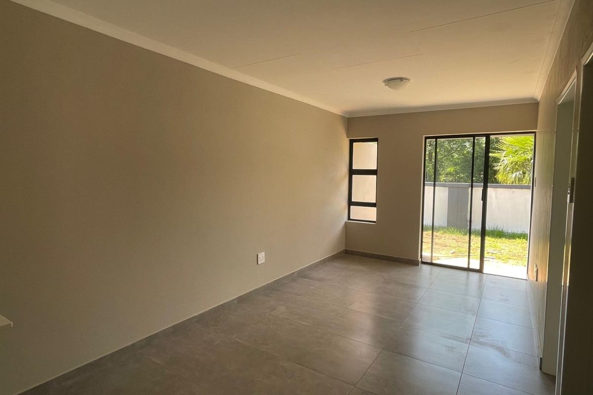 A bright, empty living room featuring neutral tiled flooring, a sliding glass door leading to the garden, and modern casement windows.