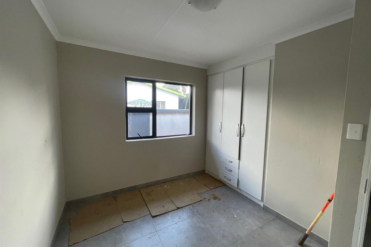 A clean, empty bedroom featuring neutral wall paint, tiled flooring, and built-in storage cupboards.