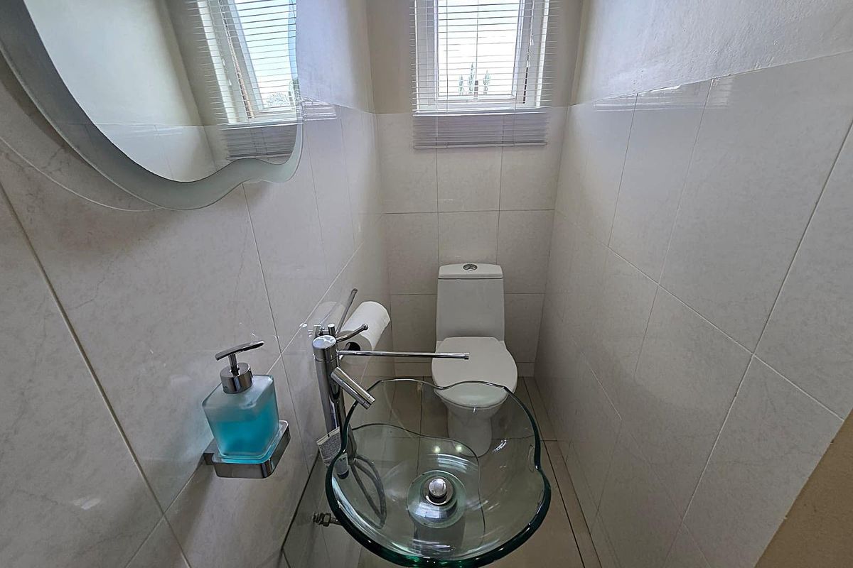 A compact guest bathroom featuring a modern glass vessel sink, wall-mounted mirror, and a standard toilet with tiled walls and flooring.