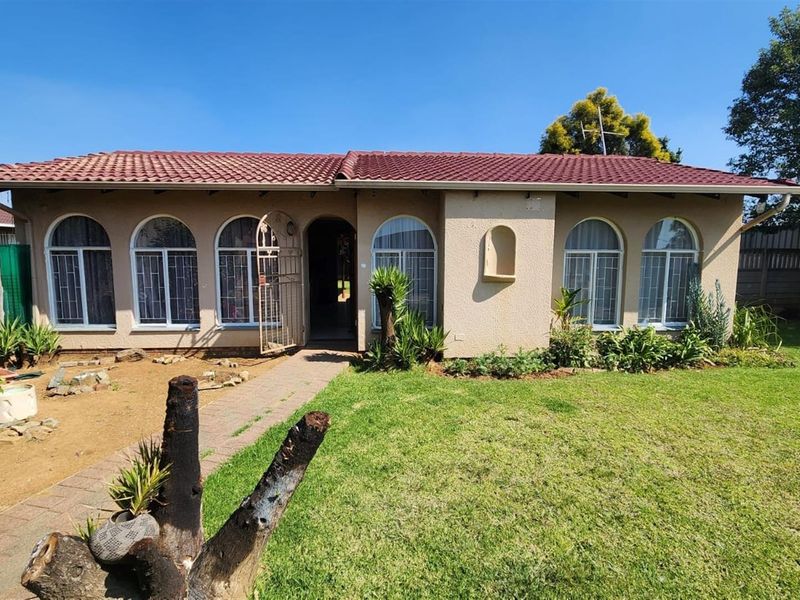 Front view of a single-story house featuring a tiled roof, arched windows, and a paved entrance path set within a landscaped garden.